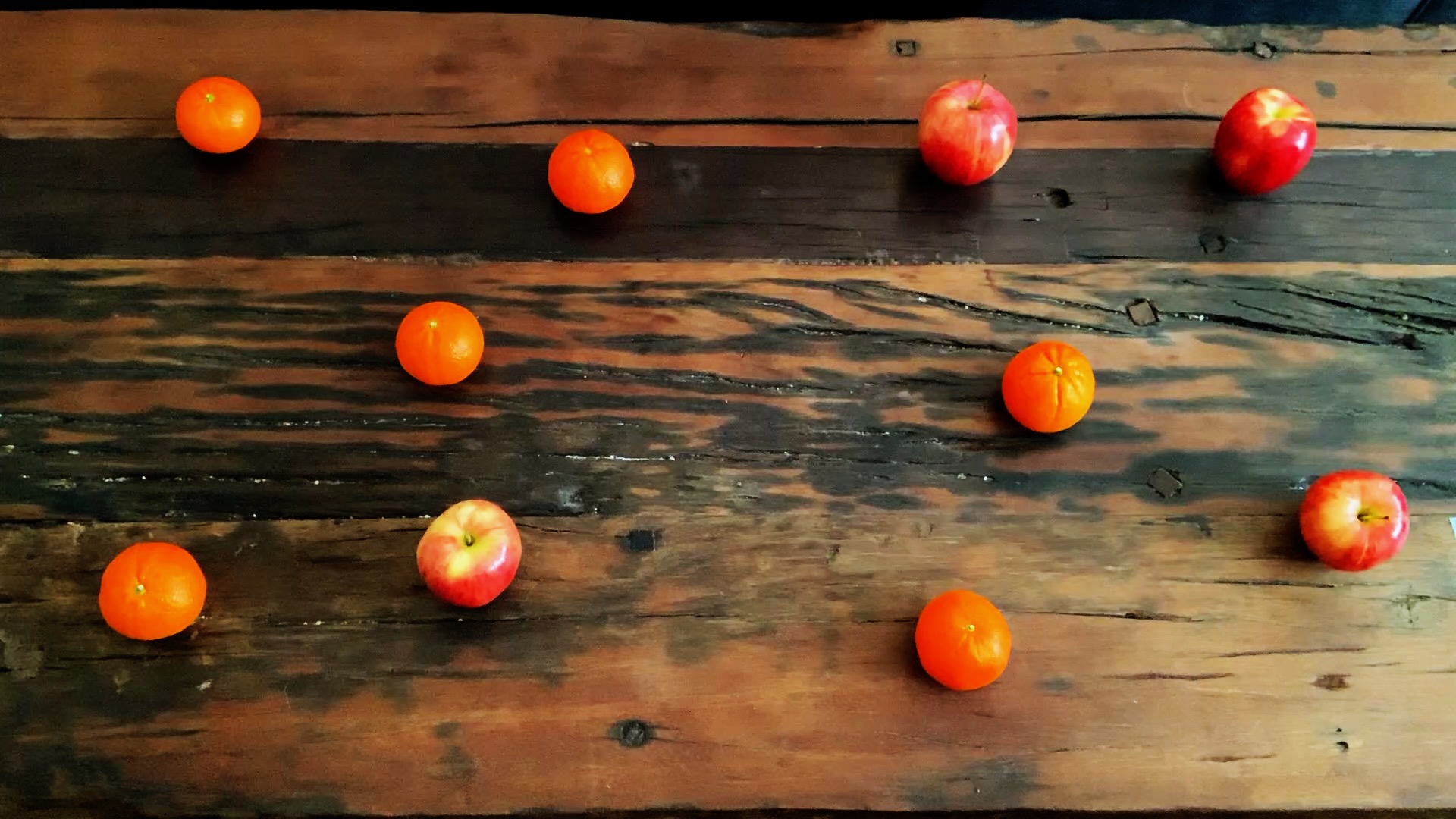Apples and oranges arranged on a table with most of the apples on the right side